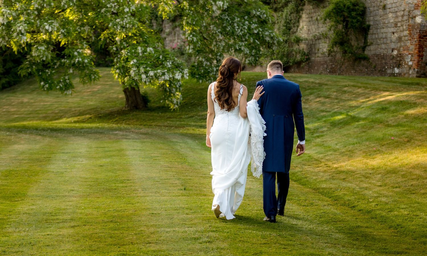 Couple walks hand in hand across expansive green lawn at historic venue.