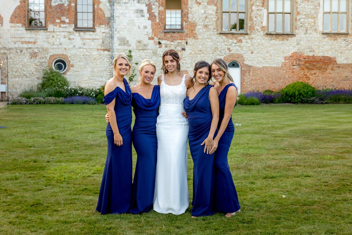 Wedding party in navy blue and white attire poses on grass near historic venue.