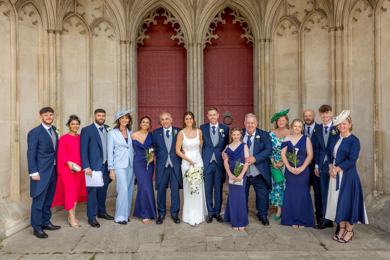 Wedding party group photo lined up against stone cathedral wall with gothic architecture.