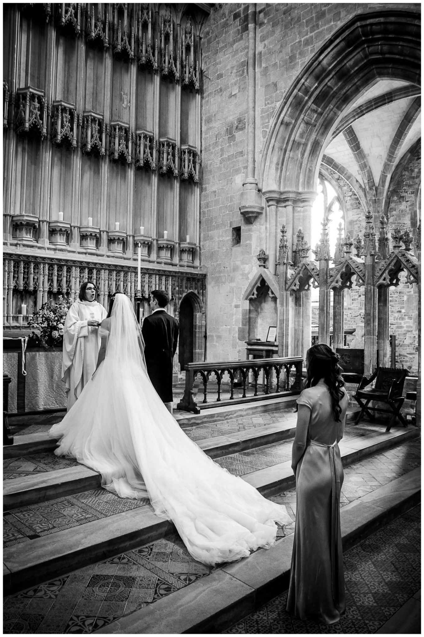 Black and white wedding photos showing a bride in a flowing gown with train walking through a Gothic church corridor.