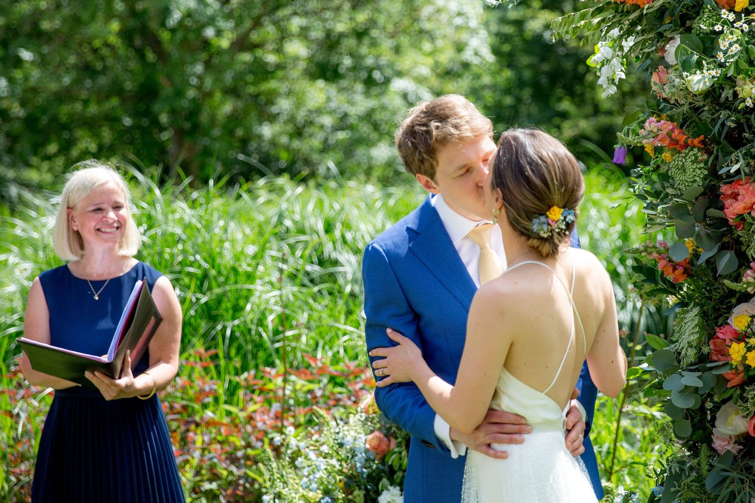 A couple shares a romantic moment during their outdoor garden wedding ceremony while an officiant holds a book.