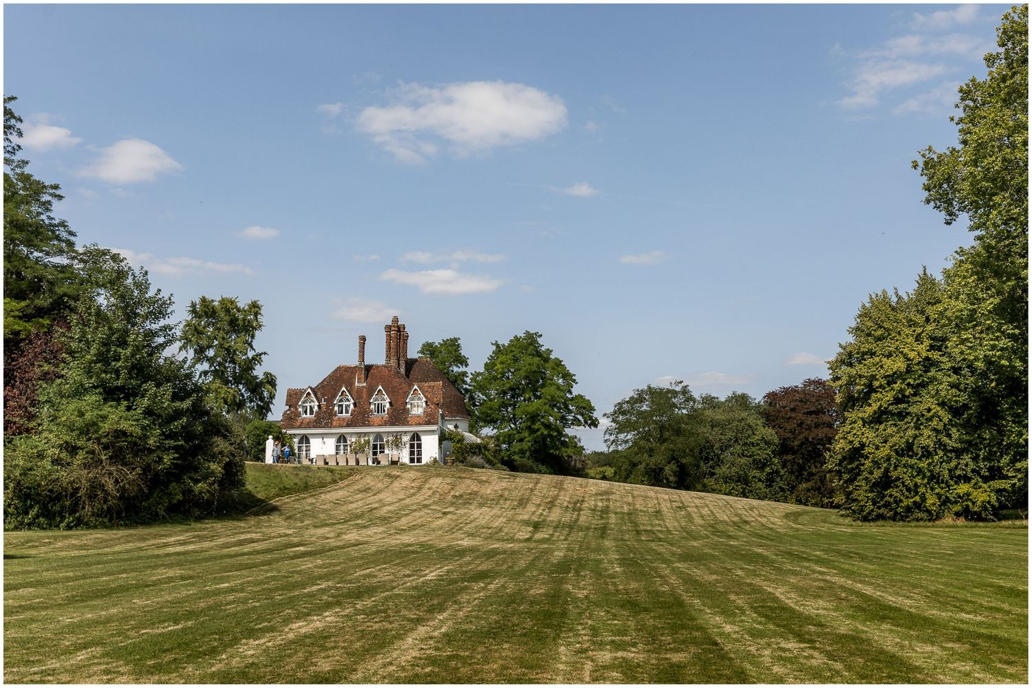 Panoramic view of a historic house on a hilltop with well-manicured green lawn under blue sky.