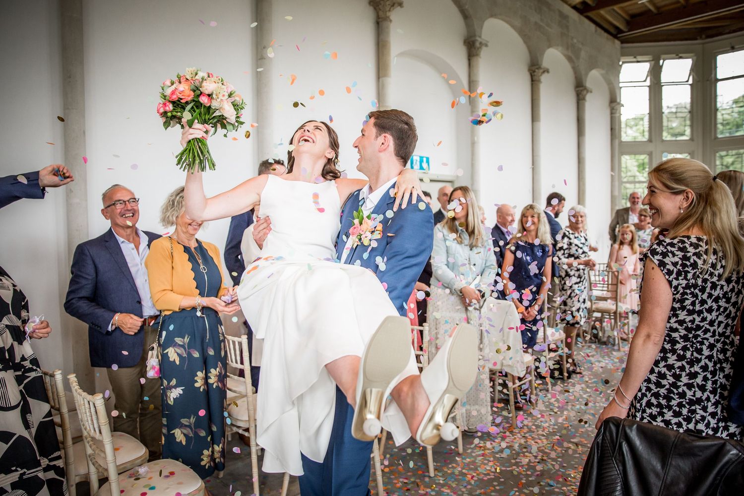 Wedding guests celebrate during an outdoor reception at a stately venue with floral arrangements.