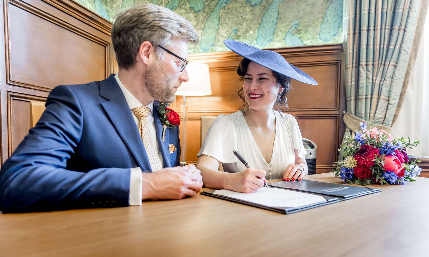 Documents being signed at an elegant wooden desk during a formal ceremony.
