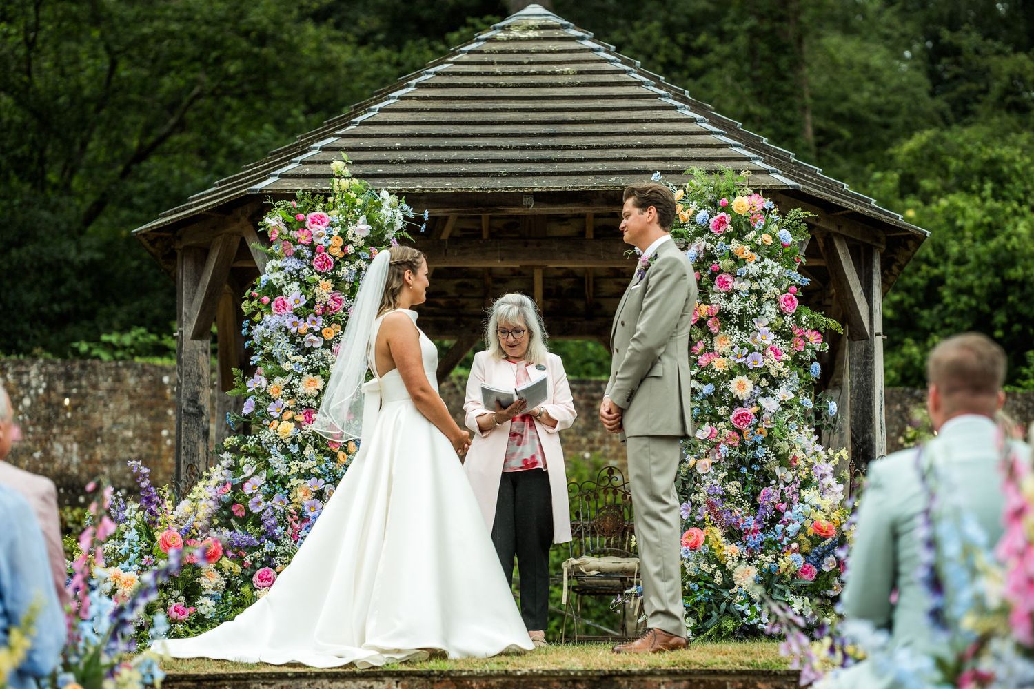 Wedding ceremony setup with colorful floral arch in a garden setting.