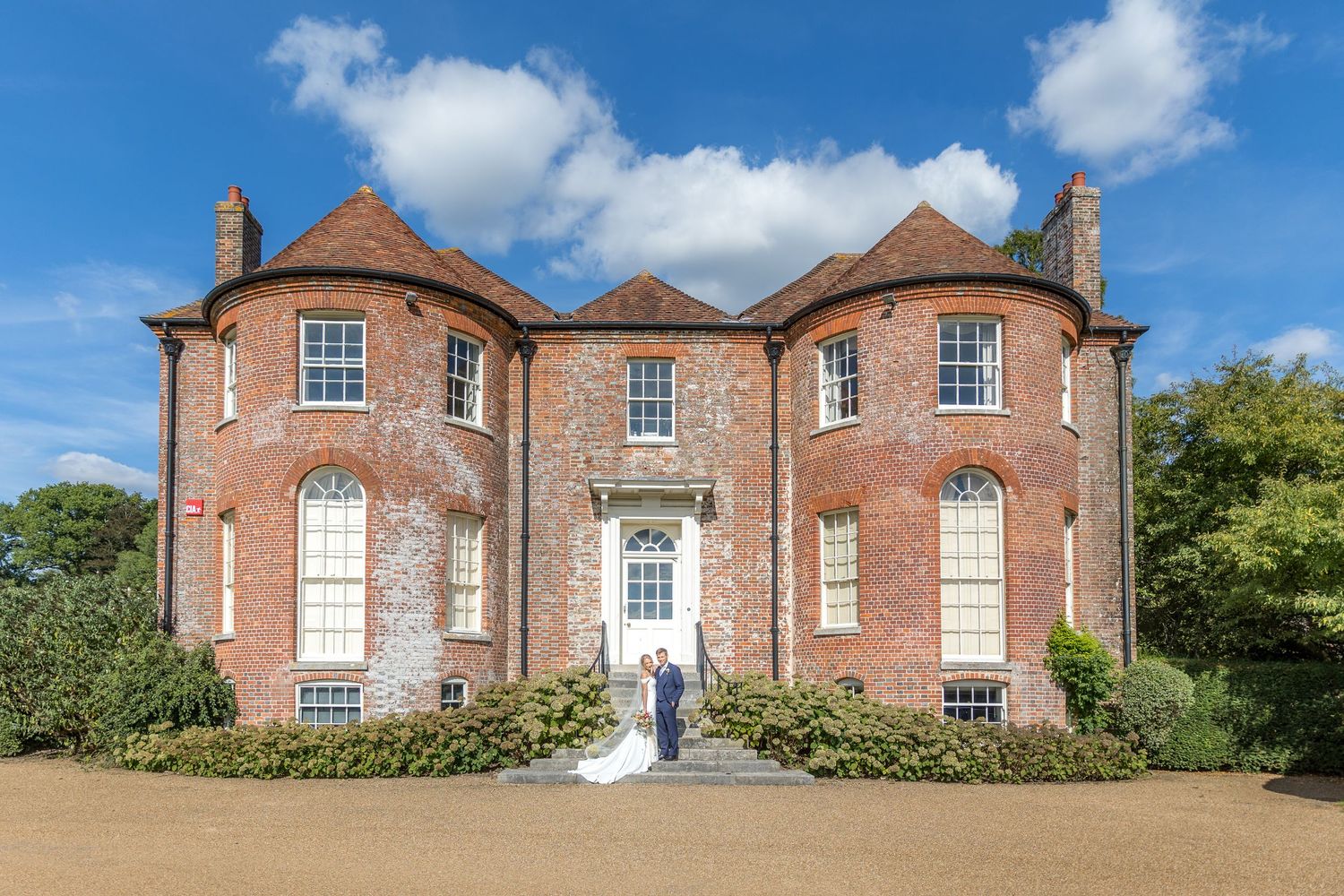 Panoramic view of a red brick Georgian manor house on a sunny day.