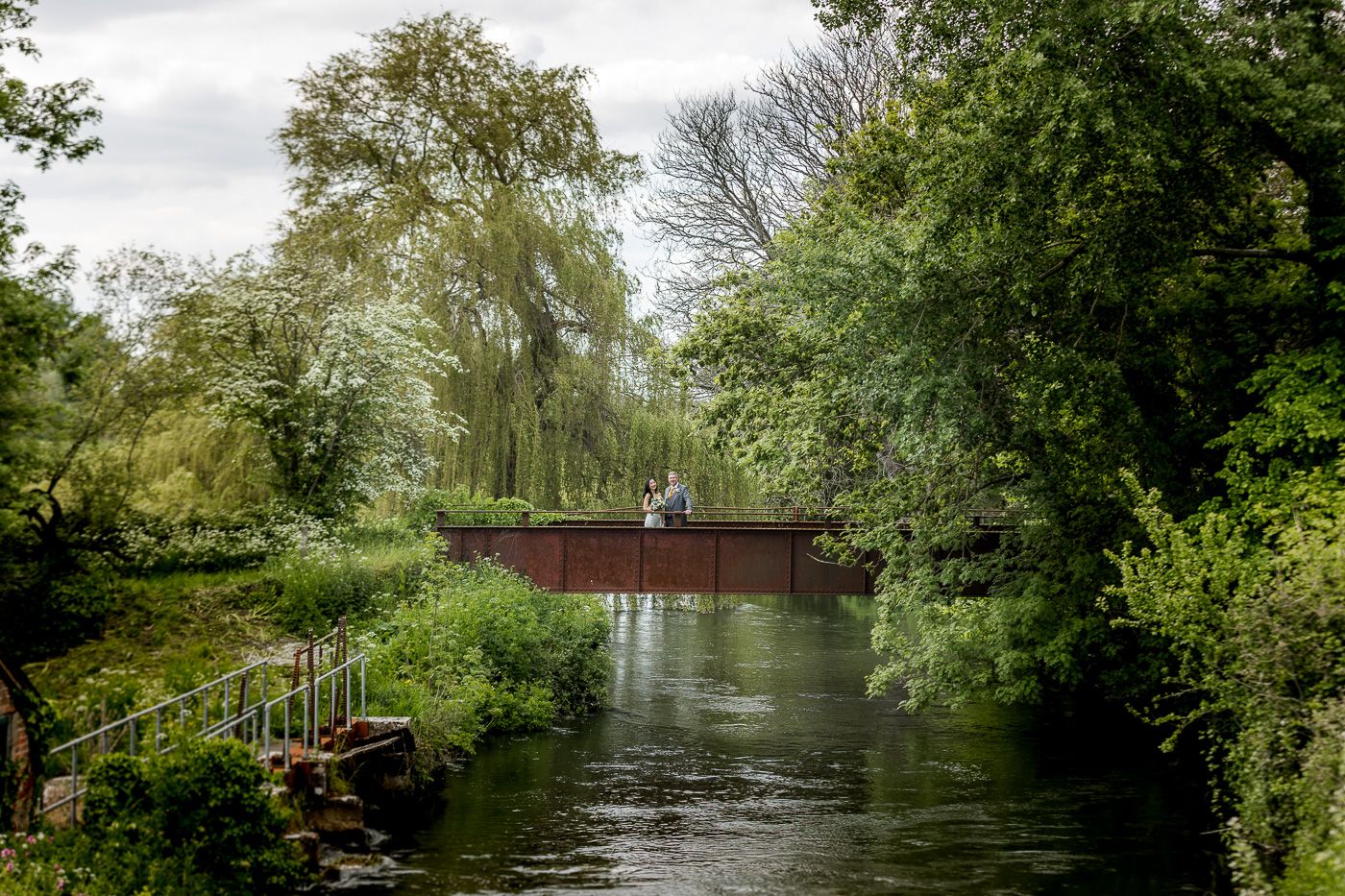 A scenic view of a wooden bridge over a tranquil river surrounded by lush green trees.