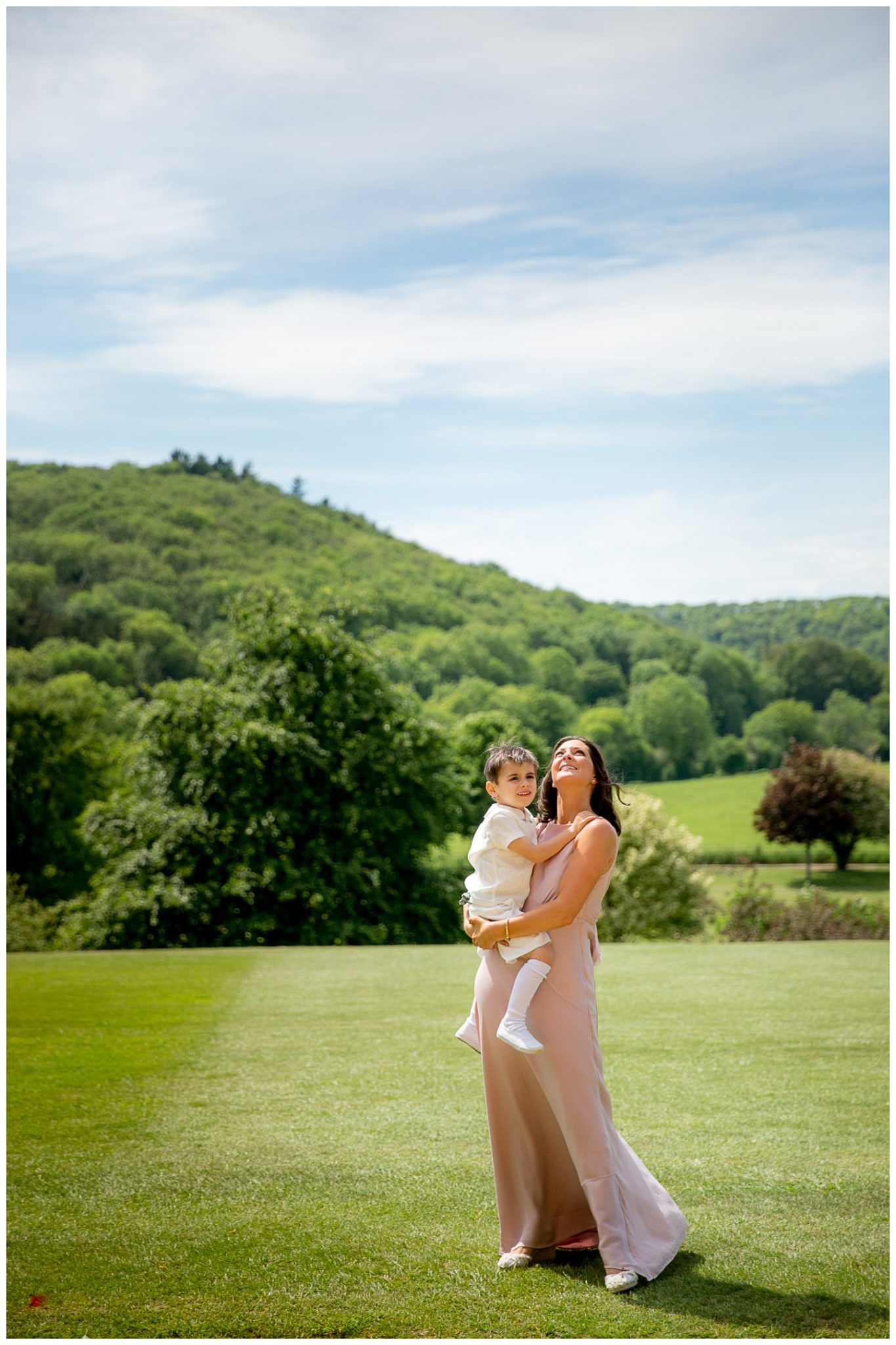 People in formal attire share a joyful moment together in a sunny meadow with rolling green hills in the background.