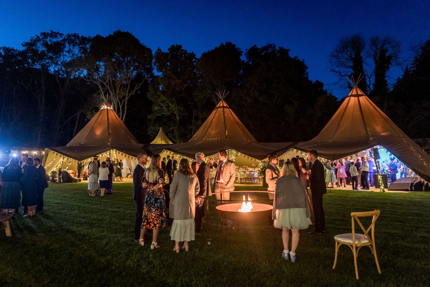 Row of lit tipi tents creating a magical evening atmosphere at an outdoor wedding venue.