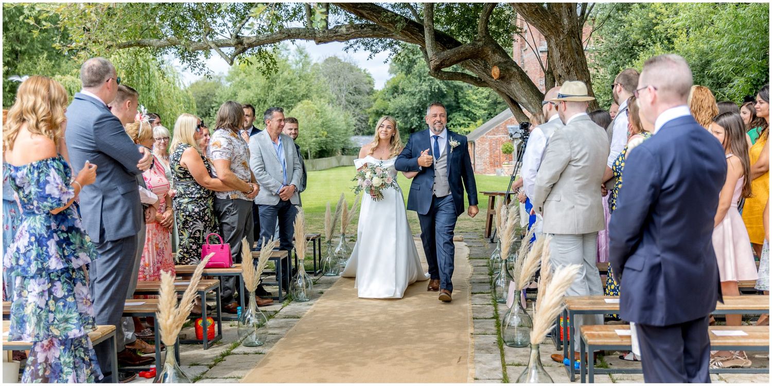 Wedding party and guests enjoy outdoor garden reception under trees.