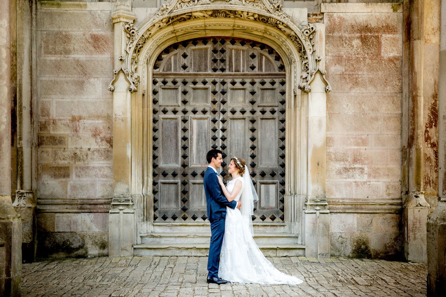 Wedding couple in front of the main doors for their portrait photographs at Highcliffe Castle, Hampshire wedding venue.