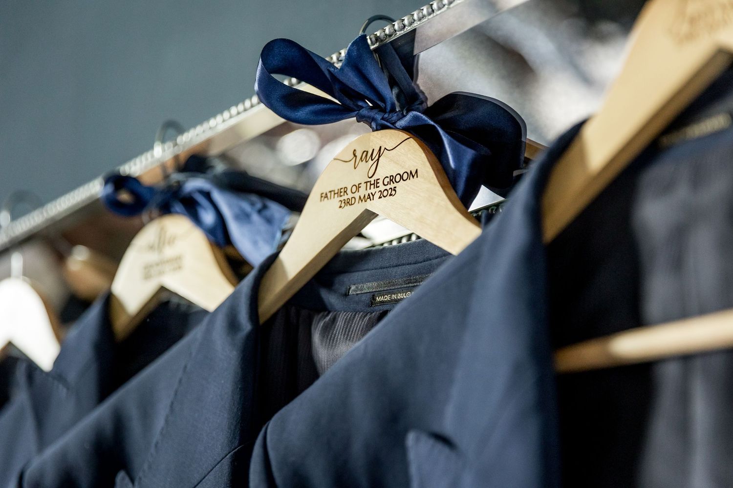 Navy blue suits with matching bow ties hanging on wooden hangers.