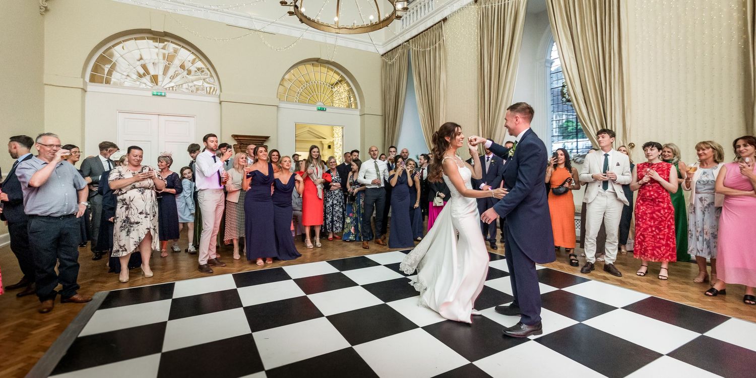 A wedding celebration in an elegant ballroom with black and white checkered floors and ornate decor.