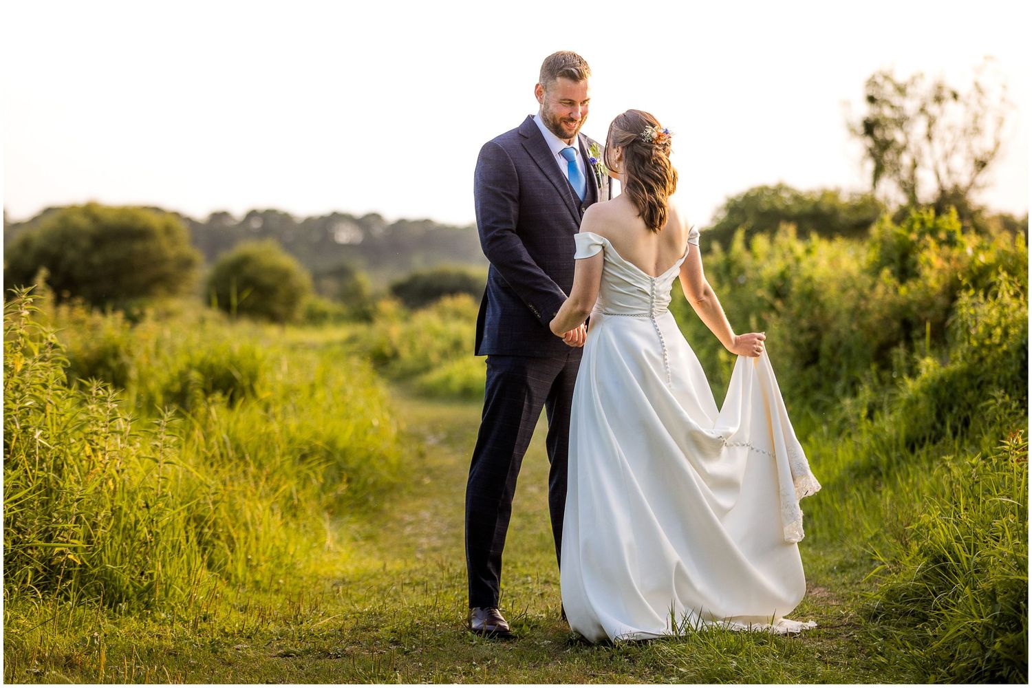 Bride and groom face each other for a wedding portrait photograph at golden hour, in the water meadows at Sopley Mill