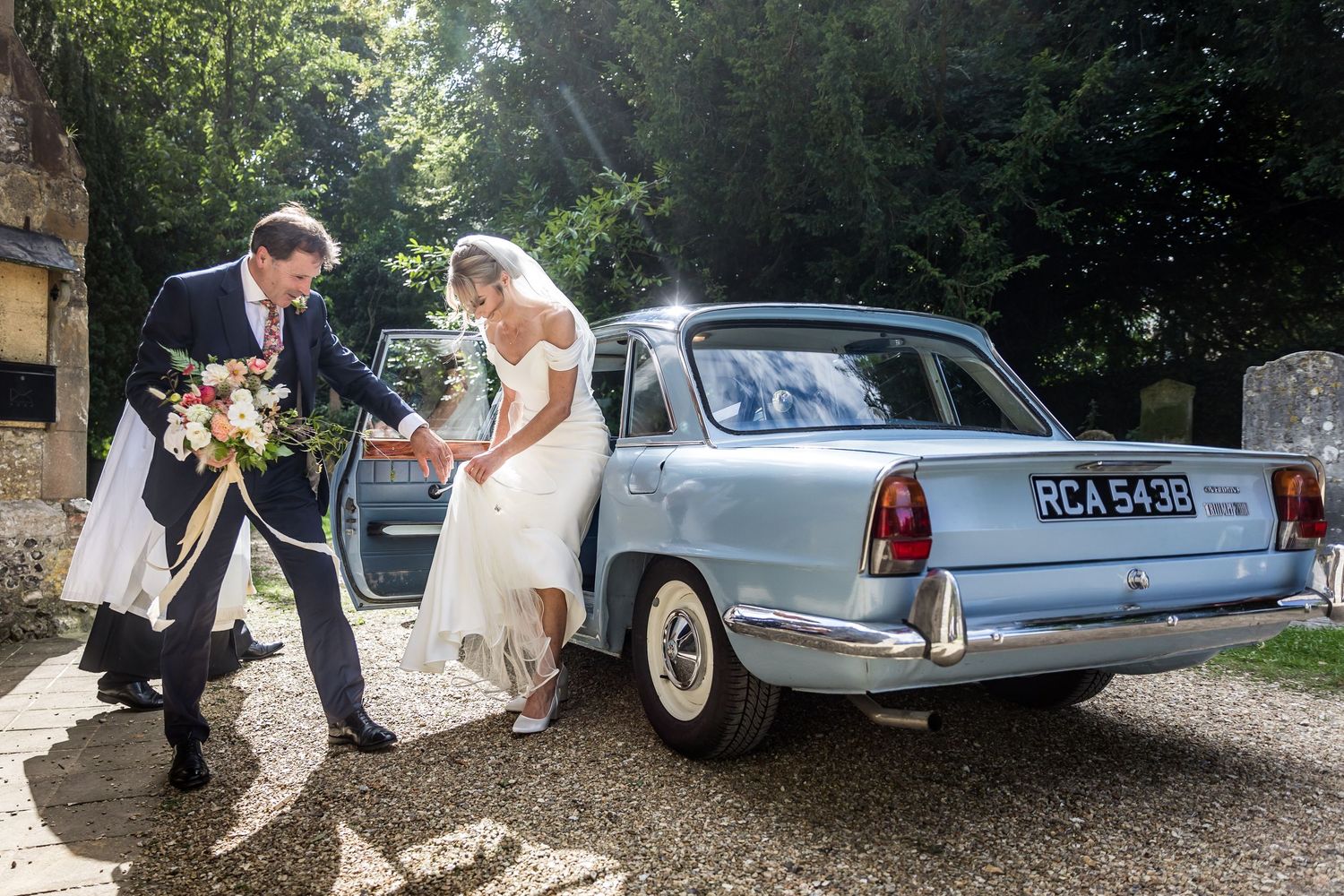 Classic vintage wedding cars parked outside historic stone church.