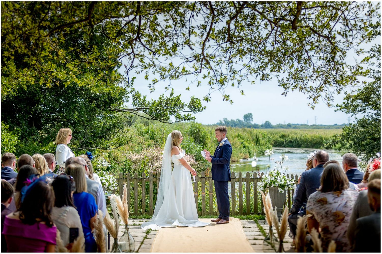 Panoramic view of an outdoor wedding ceremony setup with guests seated along a waterfront venue.