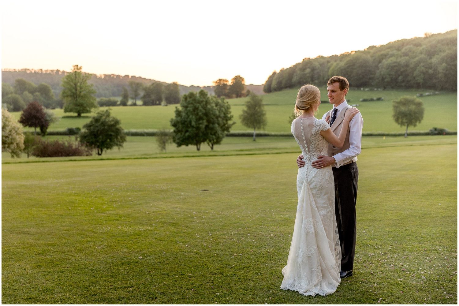 Newlyweds embracing on rolling green hills during golden hour.