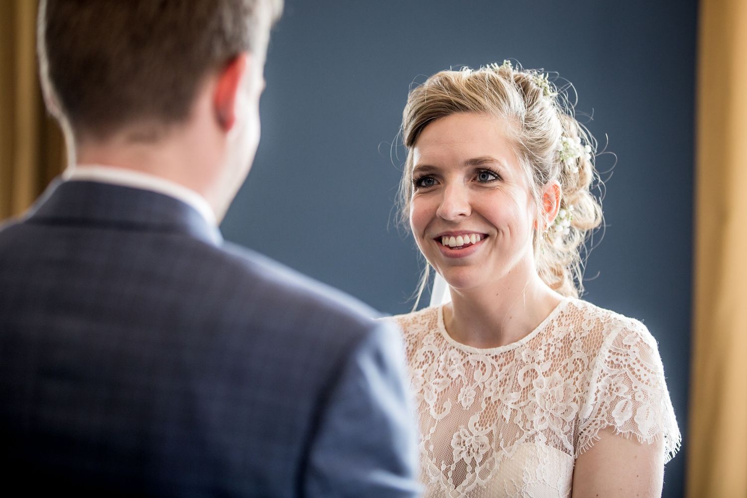 A bride in an elegant lace wedding dress smiles during a candid moment at her wedding ceremony.