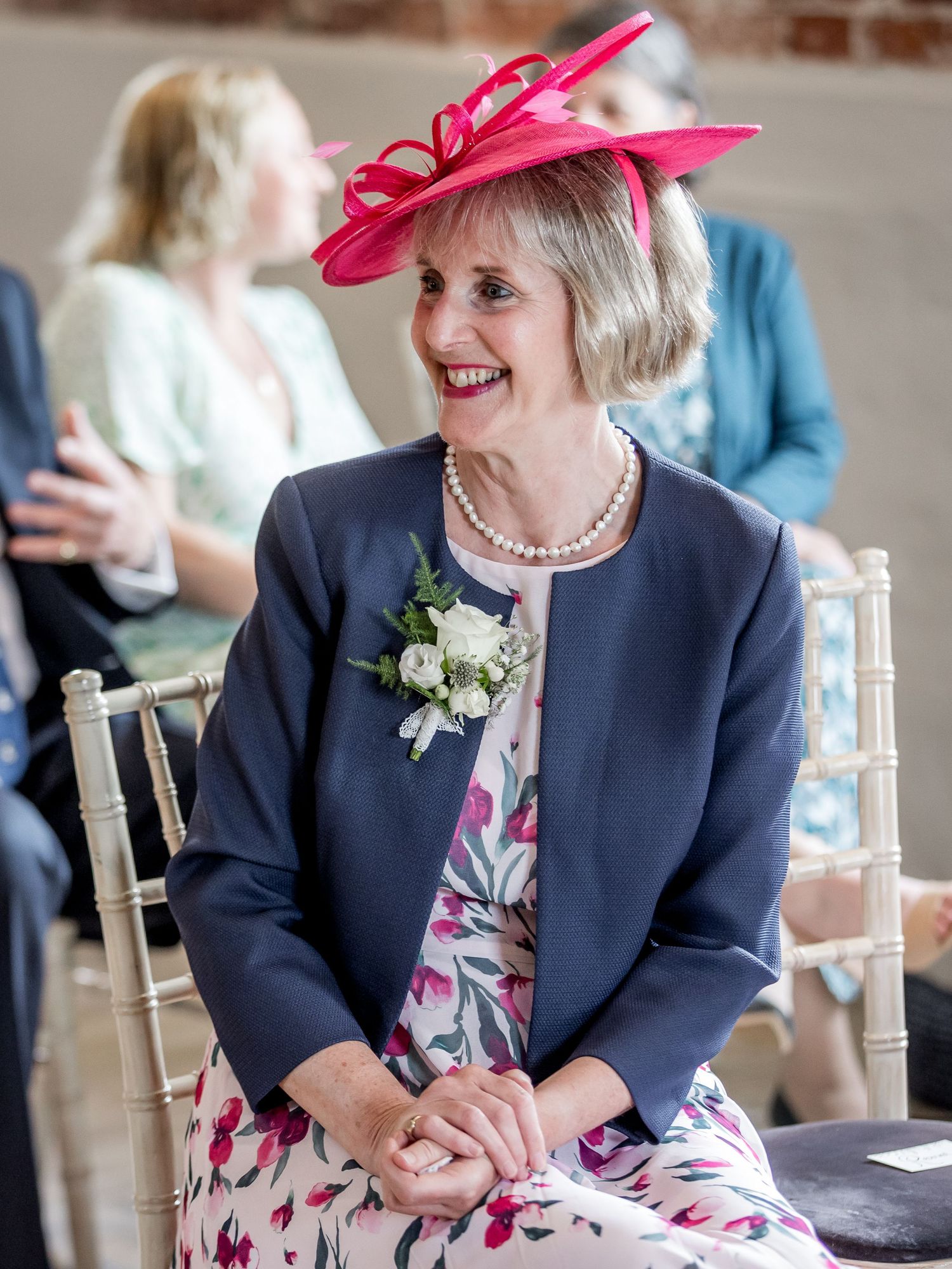 Wedding guest in a navy blazer and floral dress wearing a bright pink fascinator.