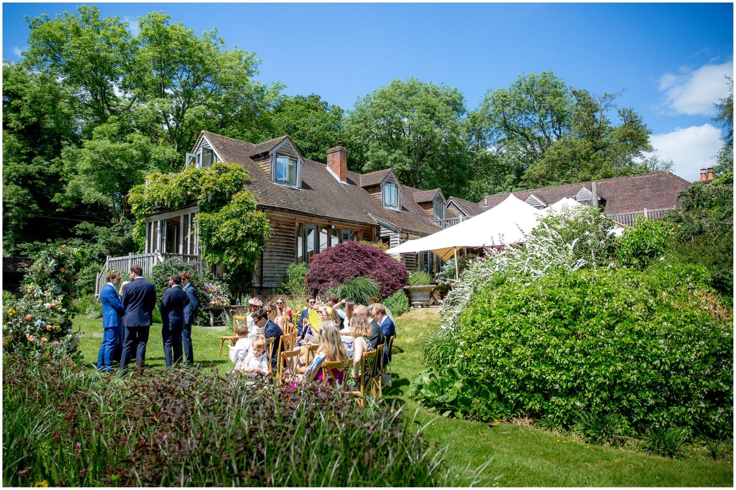 Panoramic view of a backyard wedding setup with chairs and decorations under blue summer sky.