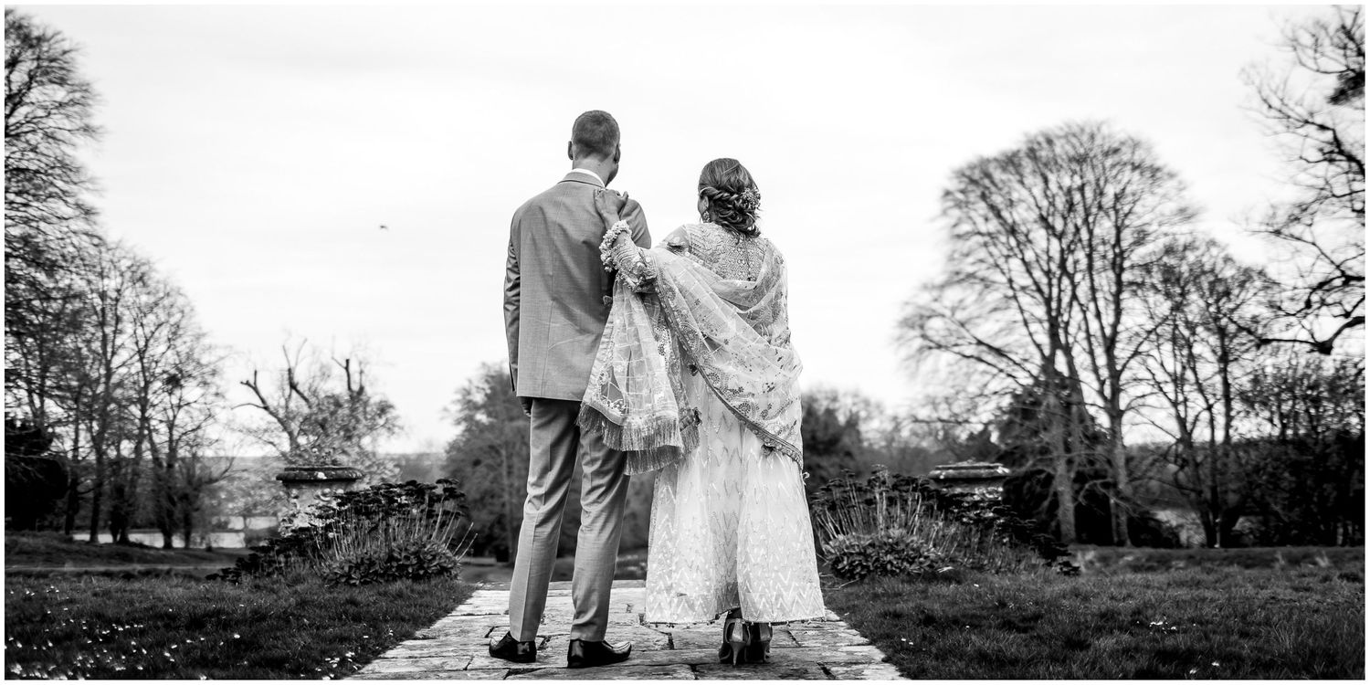 Silhouetted couple walking together through a tree-lined path during an outdoor photo session.