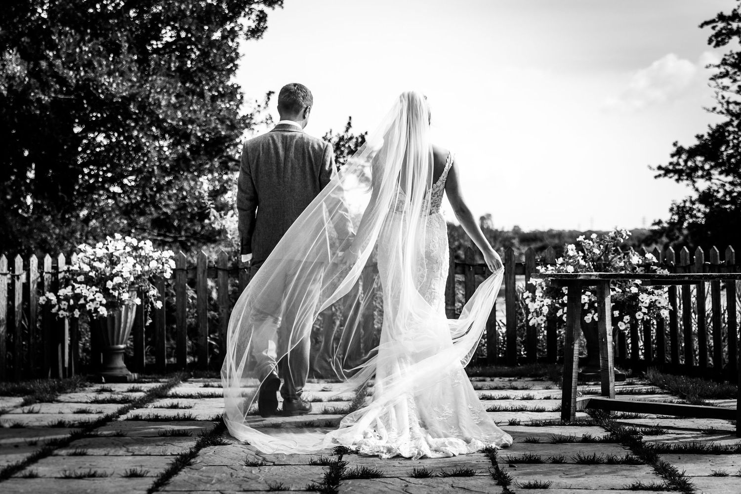 A black and white wedding photograph showing a flowing veil caught in the breeze on an outdoor terrace.