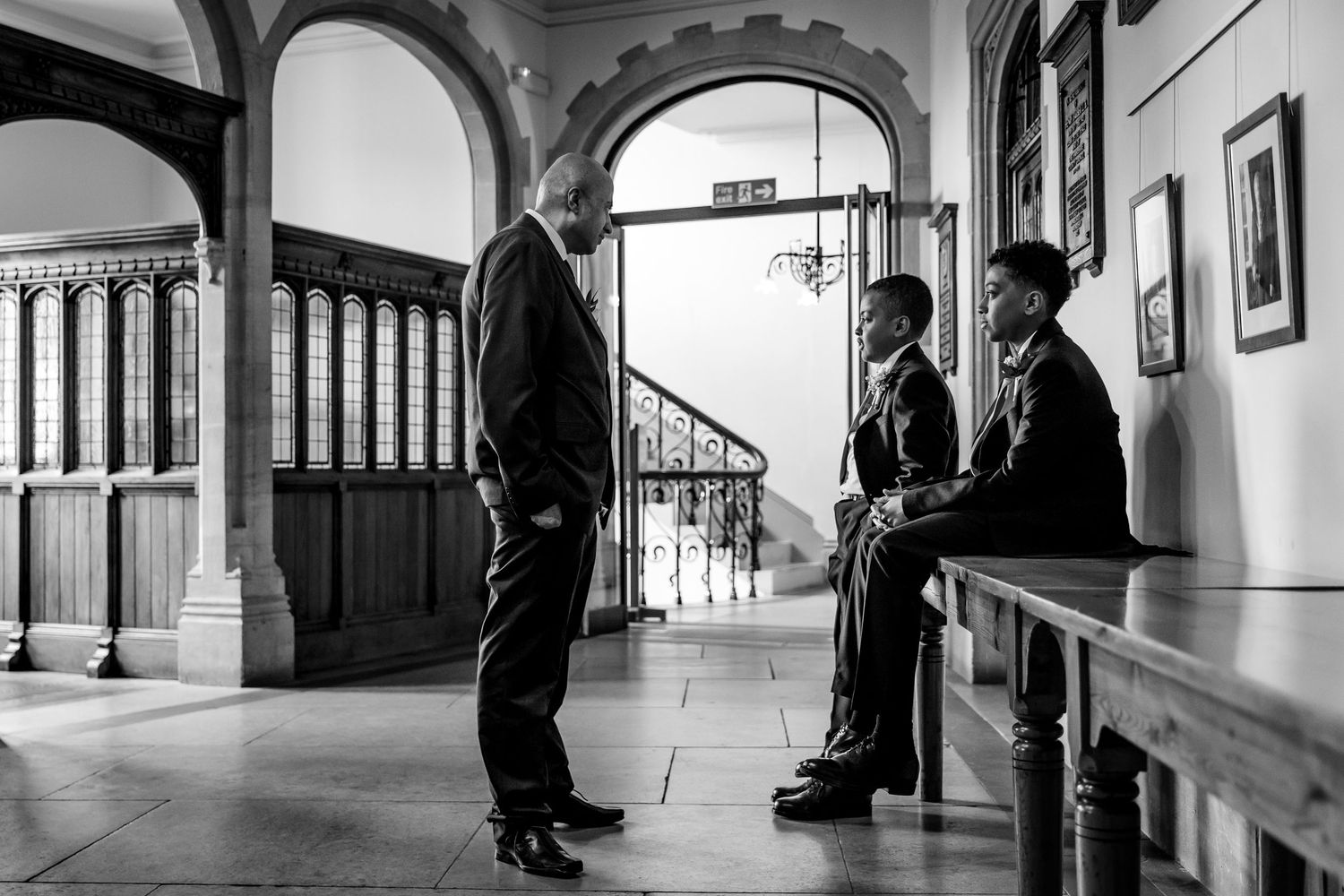 A black and white photograph showing a conversation in an ornate hallway with arched details.