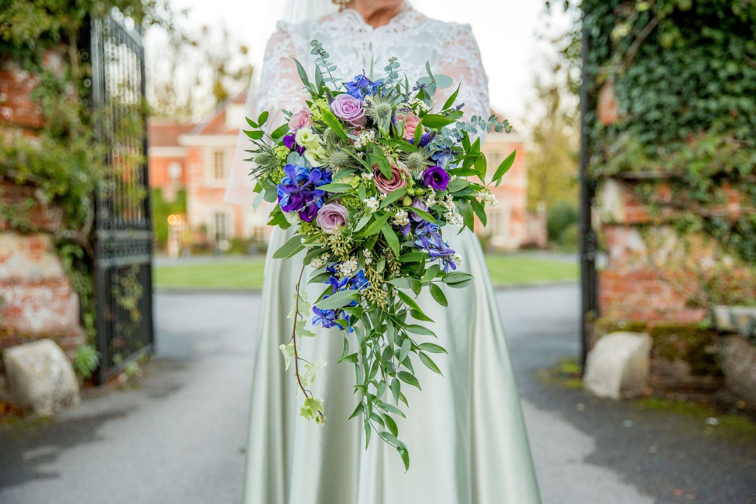 A cascading wedding bouquet with blue and purple flowers against a white dress.