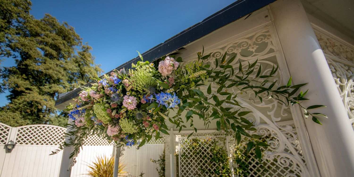 Floral arch with pink flowers and greenery decorating an elegant white outdoor wedding venue.