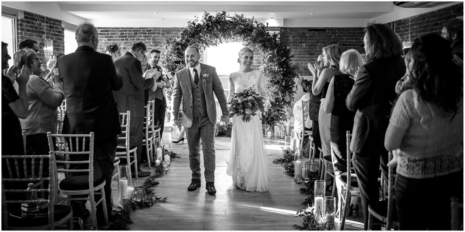 Black and white photo of newlyweds walking down the aisle after ceremony.