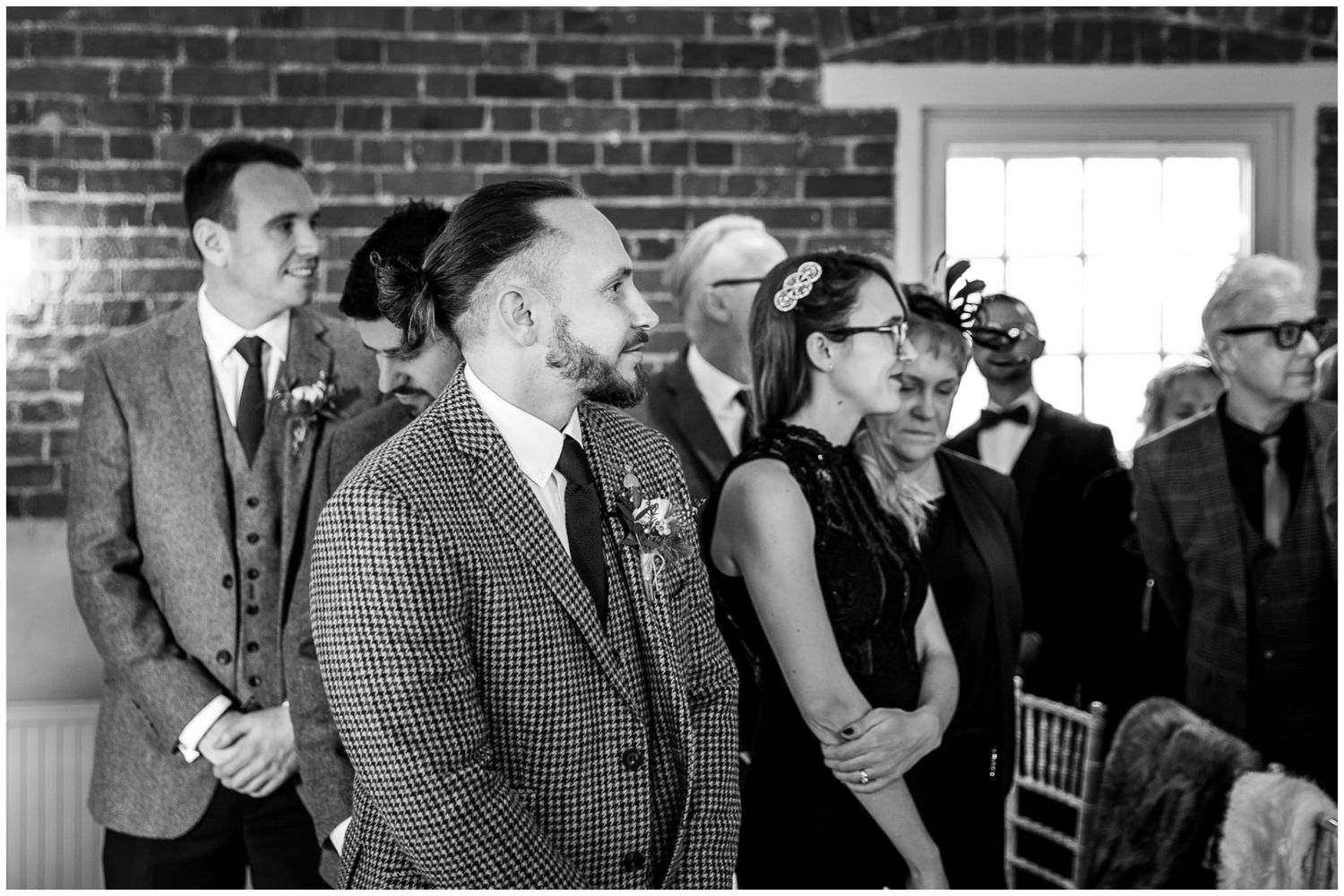 Black and white photo of wedding guests seated in rows during indoor ceremony.