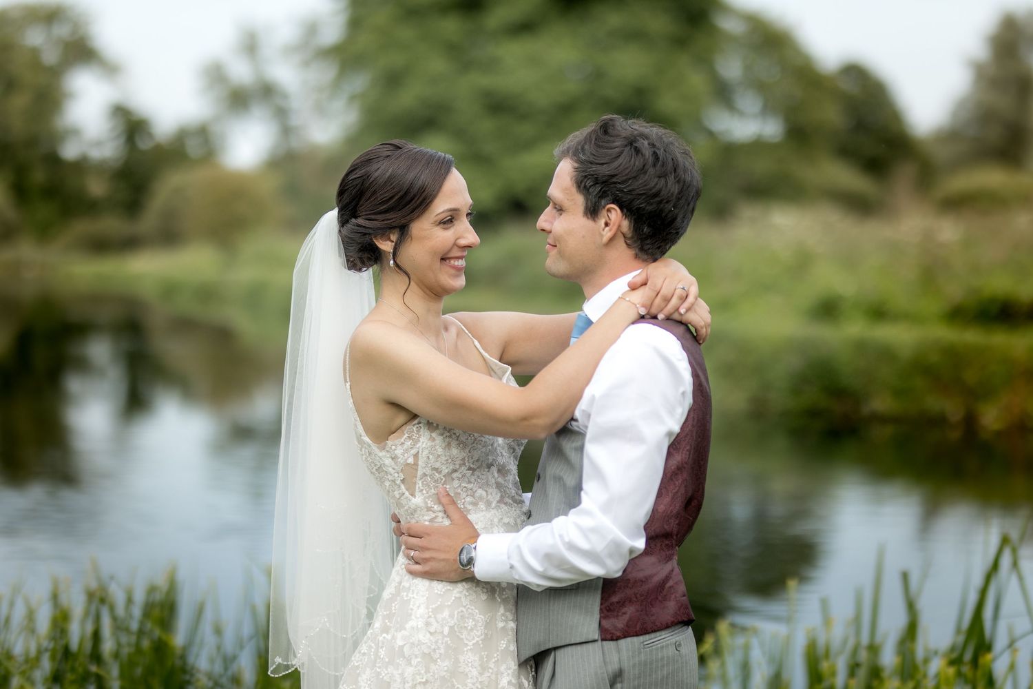 Romantic wedding photos captured by a peaceful lake with trees in the background.