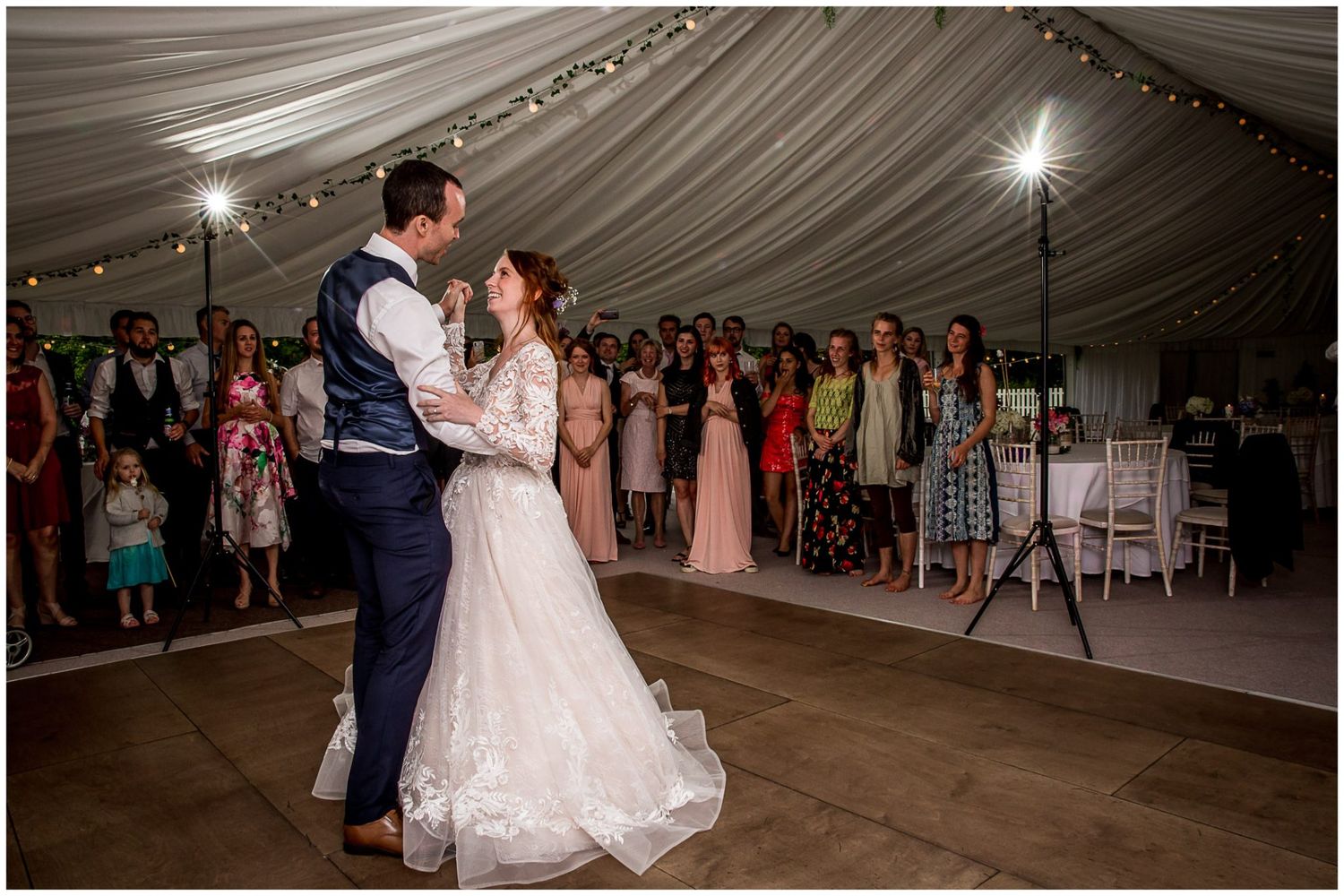 Wedding reception celebration in a large white tent with guests watching the couple's first dance.