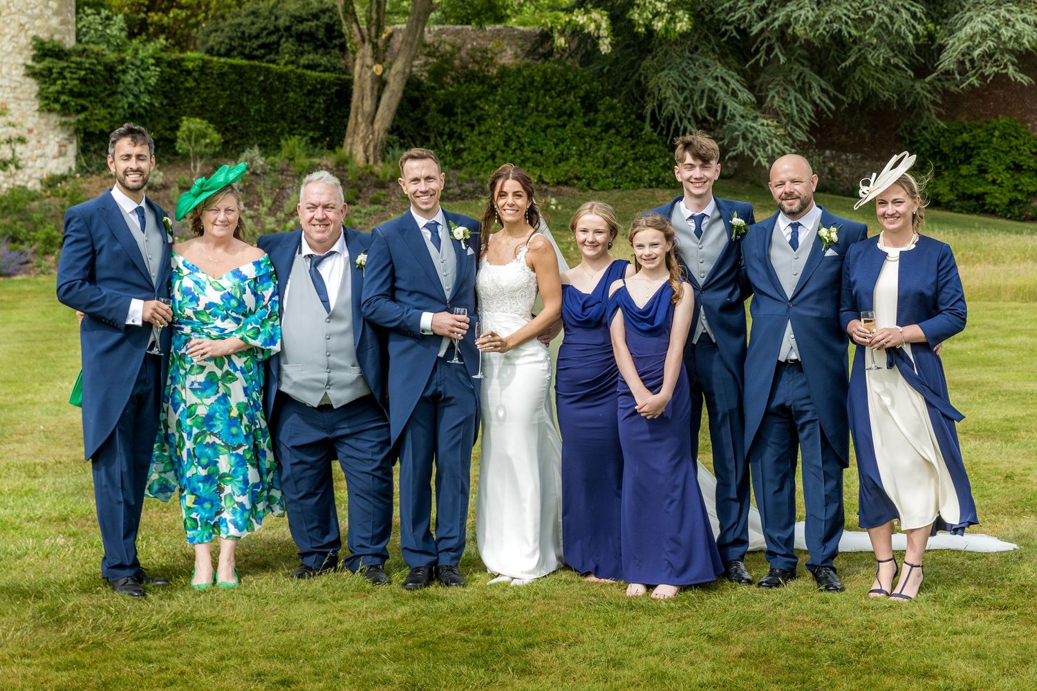Wedding party in formal attire posing on castle grounds for group photo.