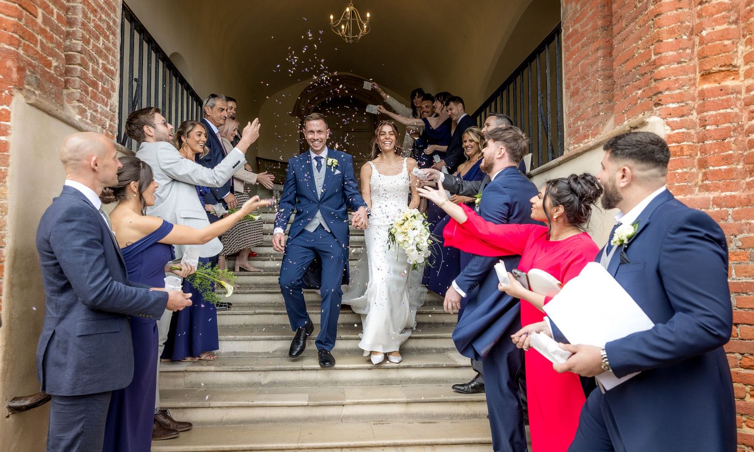 Wedding guests celebrate with confetti outside a historic brick church entrance.