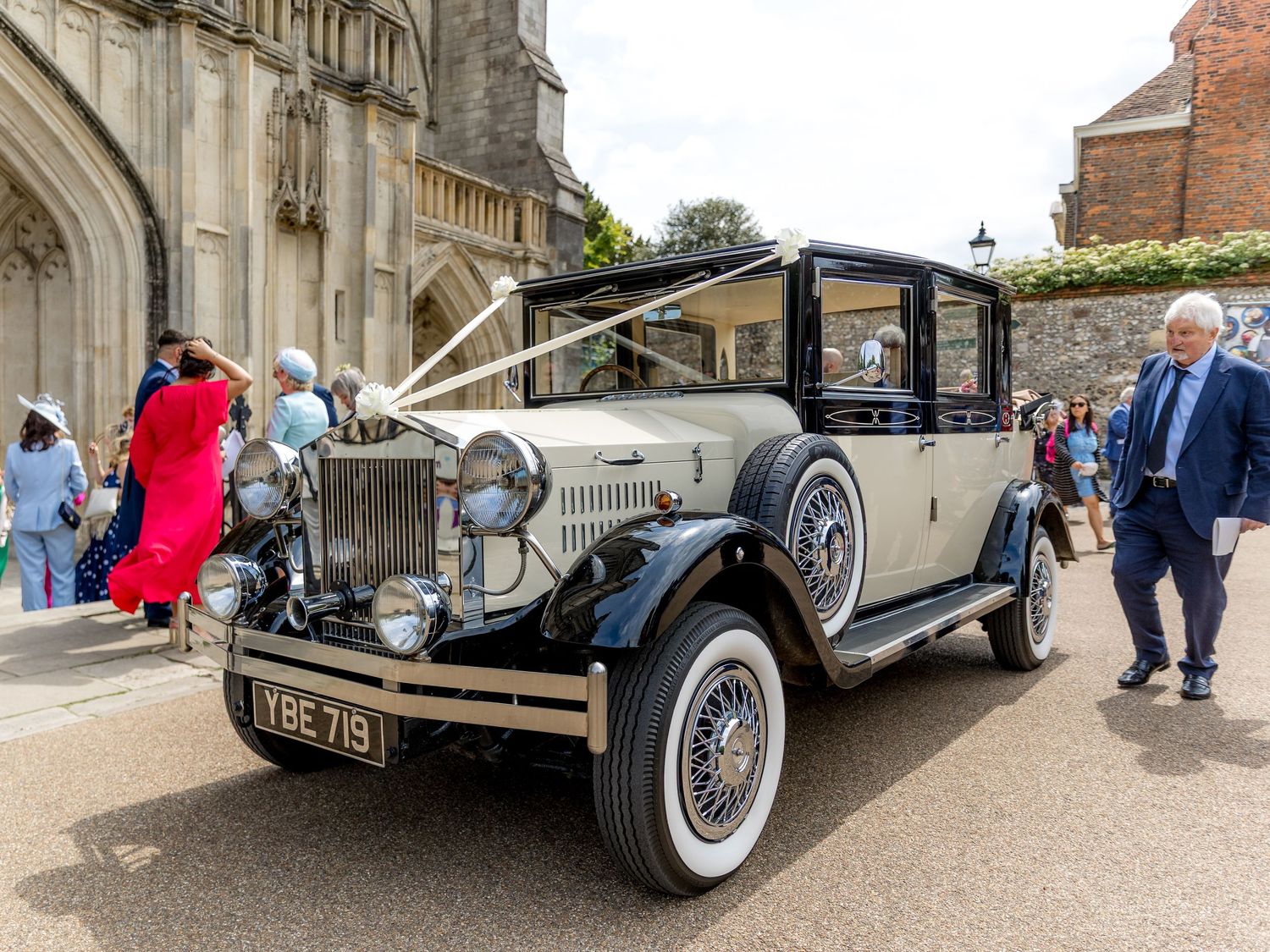 Vintage luxury cars parked outside historic cathedral for wedding transportation.