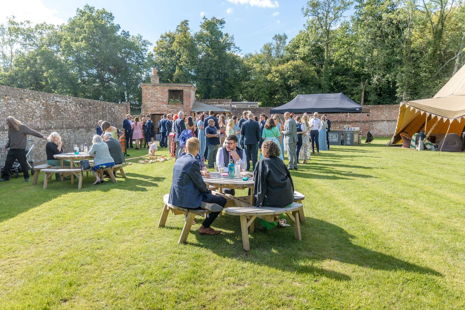 Outdoor wedding reception with picnic tables and guests enjoying the garden setting.