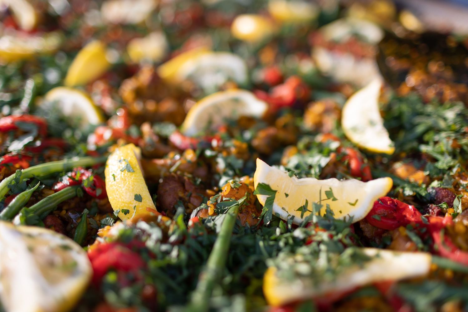 Close-up of colorful paella dish with vegetables, lemon slices and fresh herbs.