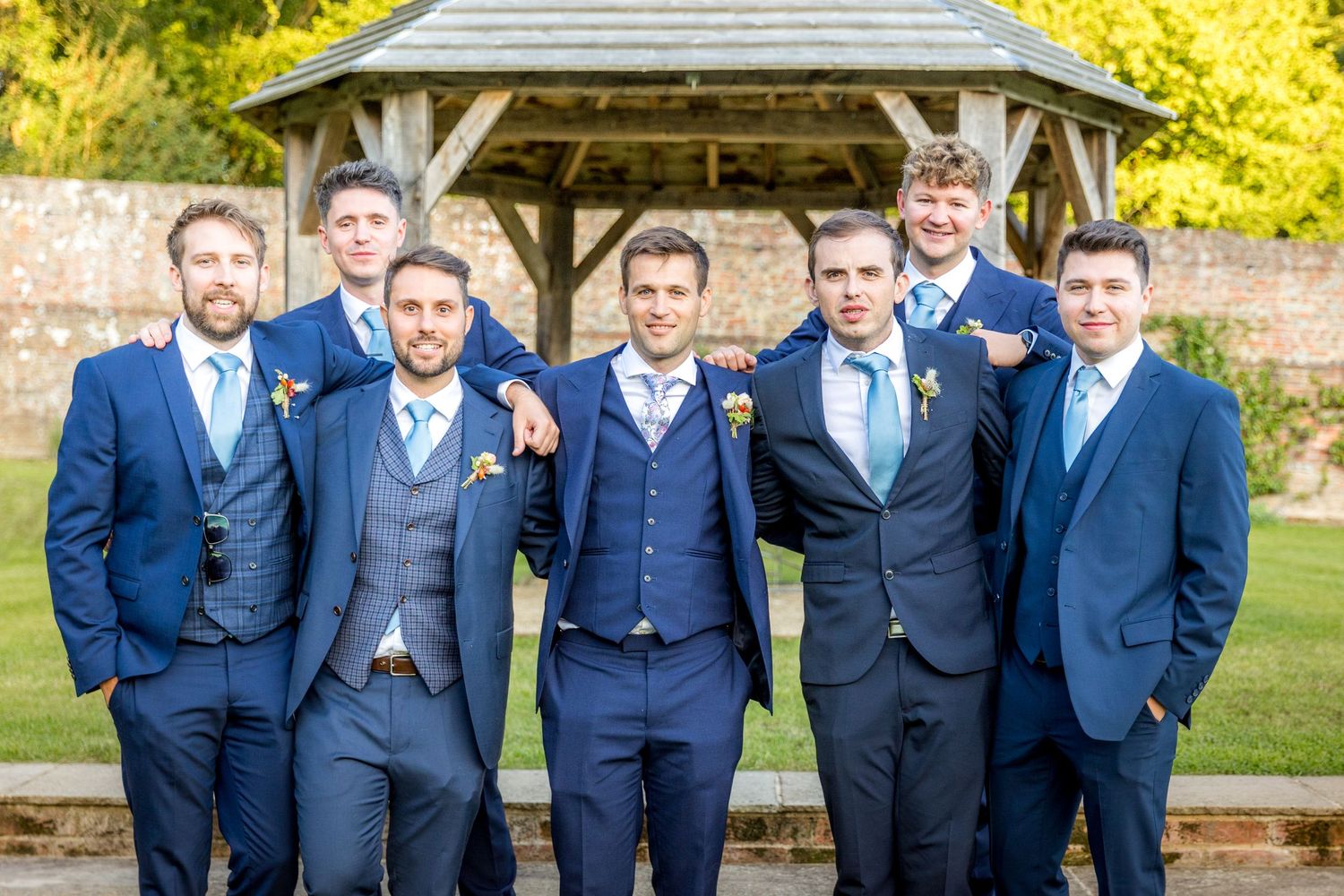 Groomsmen in matching navy blue suits and ties stand together for formal wedding photos.
