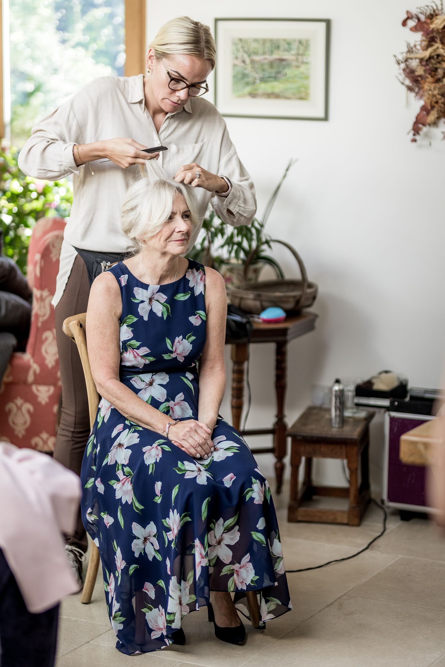 Wedding preparations with attendants in navy floral dress getting ready in a sunlit room.