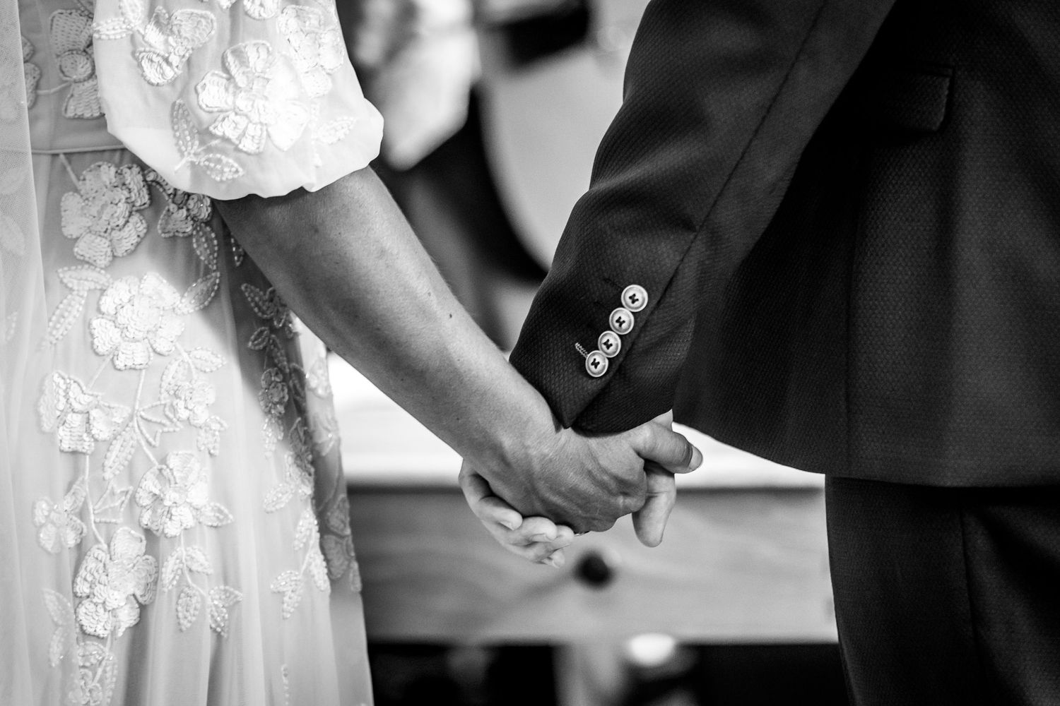 Close-up black and white photo of couple holding hands during wedding ceremony.