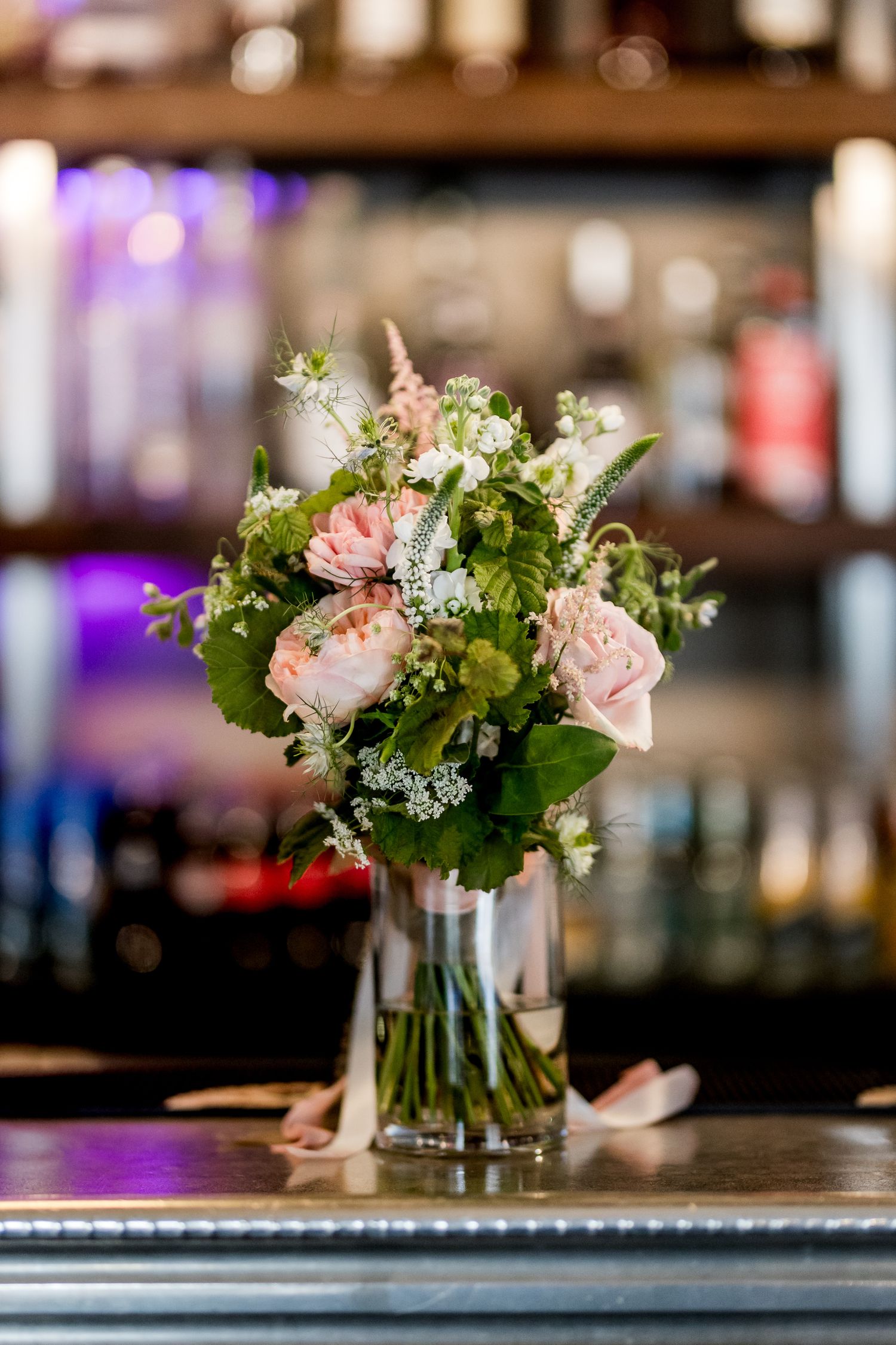 Pink and white flower centerpieces in glass vases displayed on a dark surface.