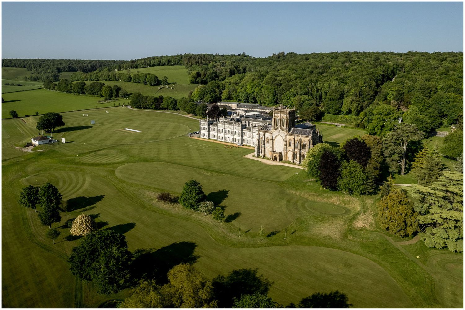 Aerial view of a stately manor house surrounded by manicured golf course and green countryside.