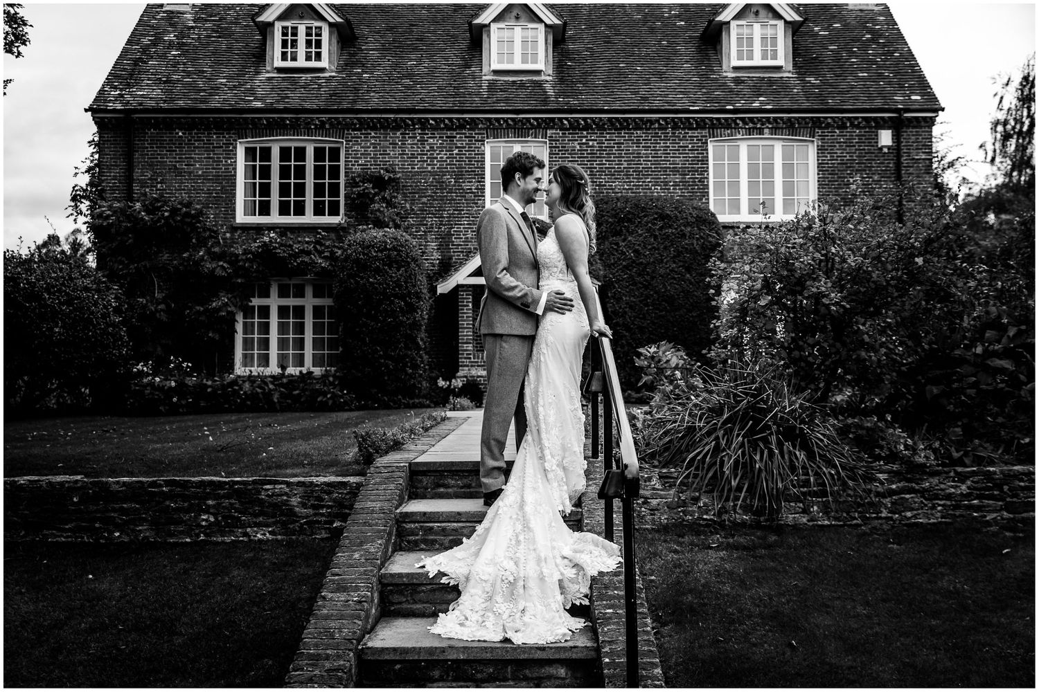 Black and white wedding portrait with bride and groom stood on stone steps outside a farmhouse at Clock Barn near Whitchurch in Hampshire