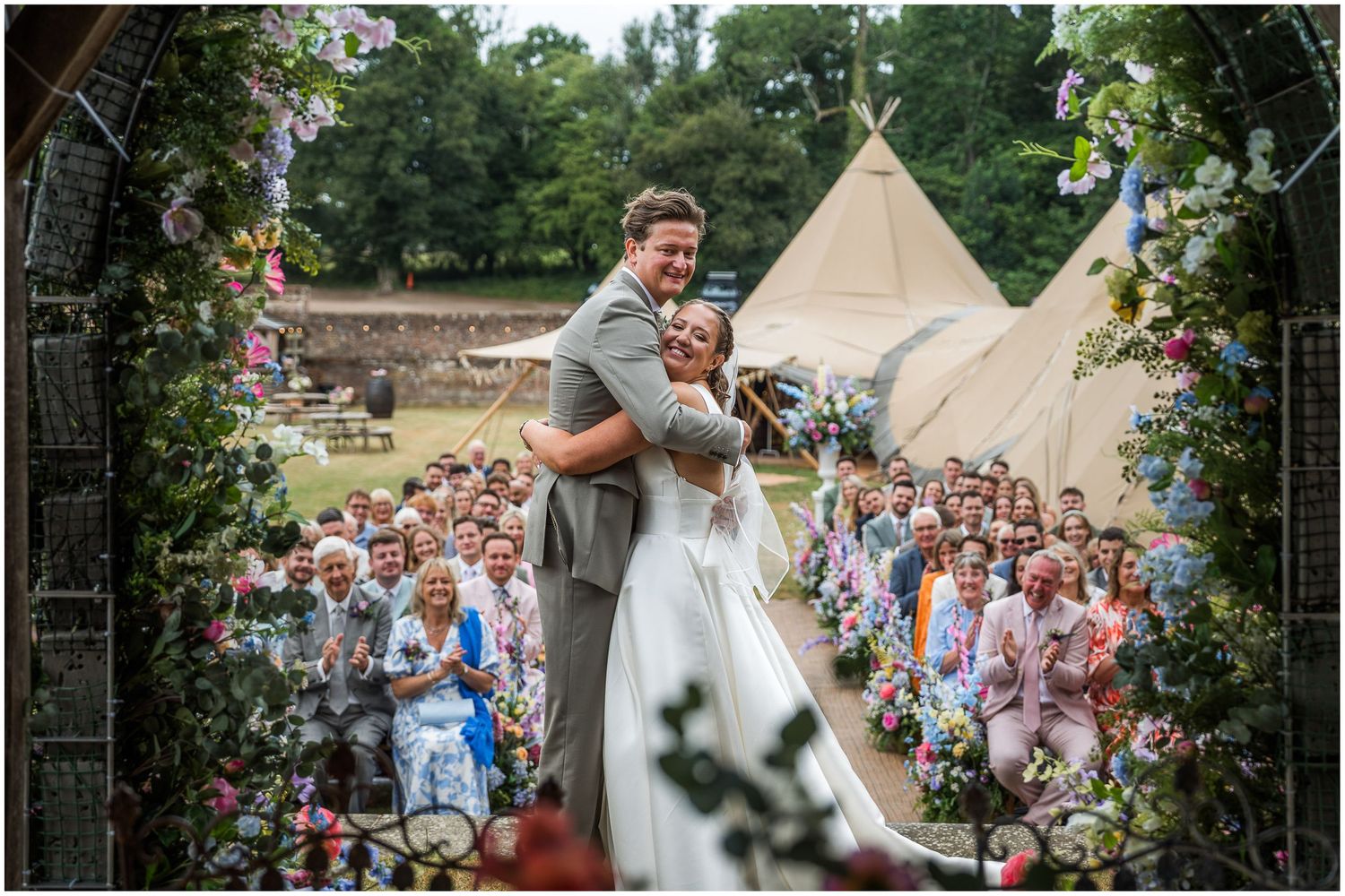 The wedding couple hug under the gazebo with wedding guests in the background