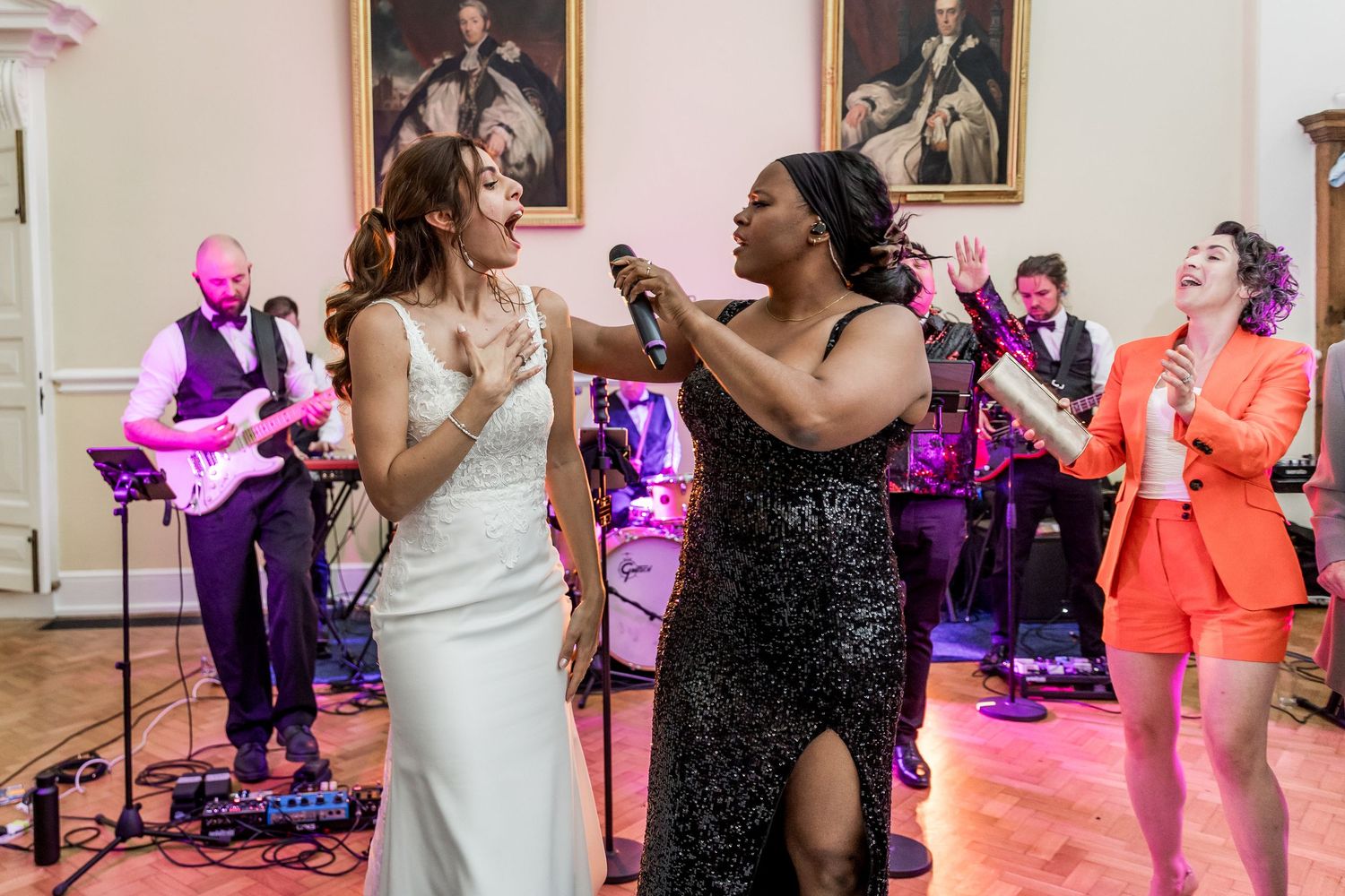 Wedding reception dance party with colorful purple lighting and live band performing.