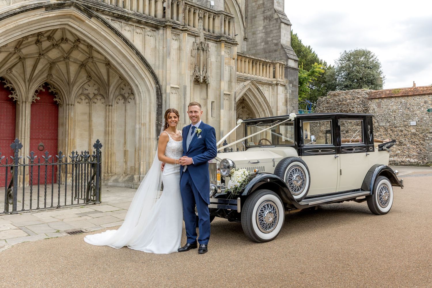 Wedding photography series with vintage car against cathedral's stone archways and red doors.