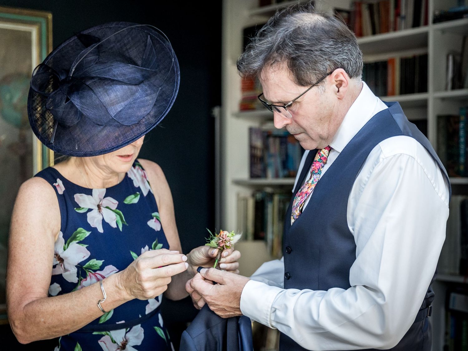 Close-up of hands pinning a floral corsage onto formal attire at a wedding.