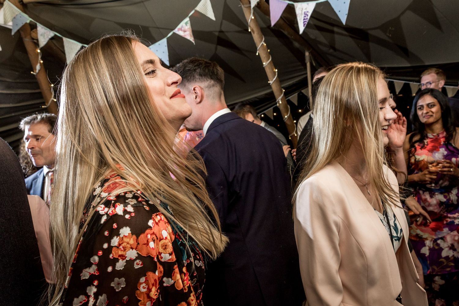 Wedding guests dance and celebrate at a lively indoor reception with decorative bunting overhead.