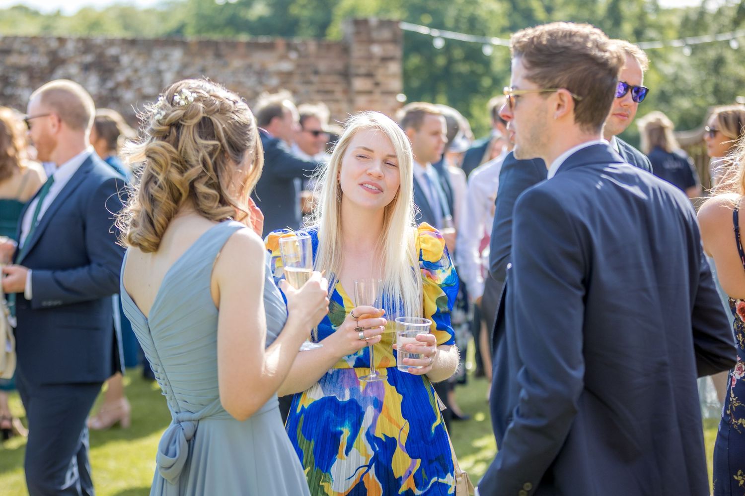 Wedding guests mingle and socialize during an outdoor reception on a sunny day.